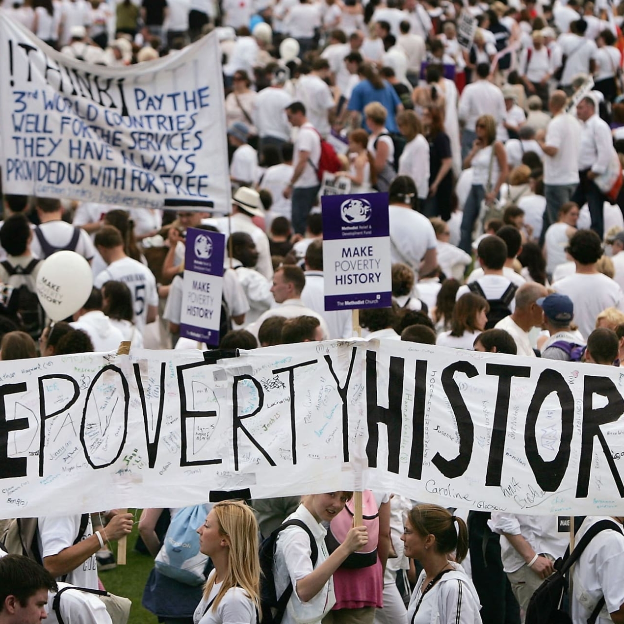 A group of people wearing white t-shirts attending a march and holding up several signs that say Make Poverty History
